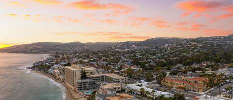 A coastal cityscape with a beach, residential buildings, and a hilly backdrop during sunset.