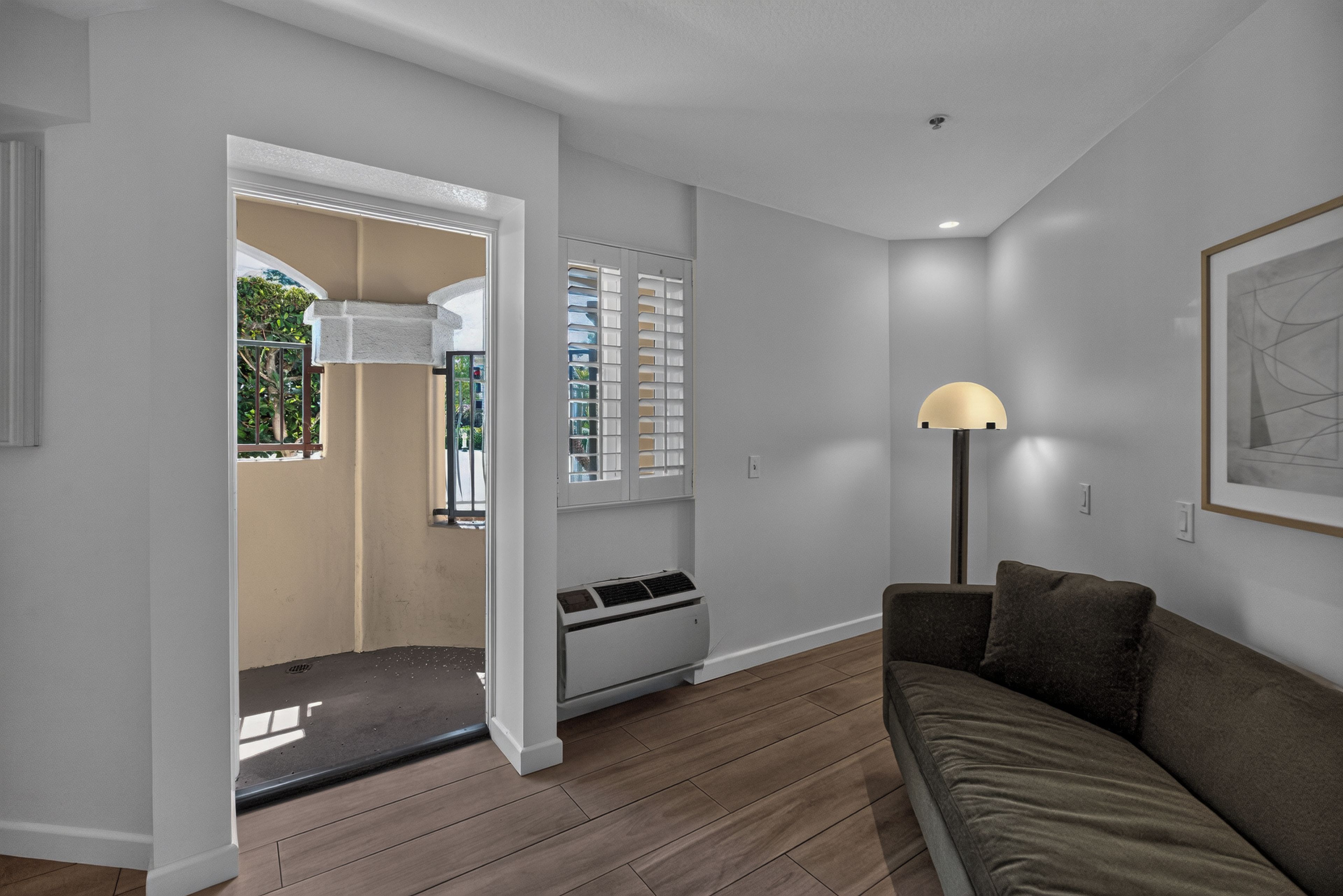 Una sala de estar moderna con piso de madera, un sofá, una lámpara y una ventana con persianas.