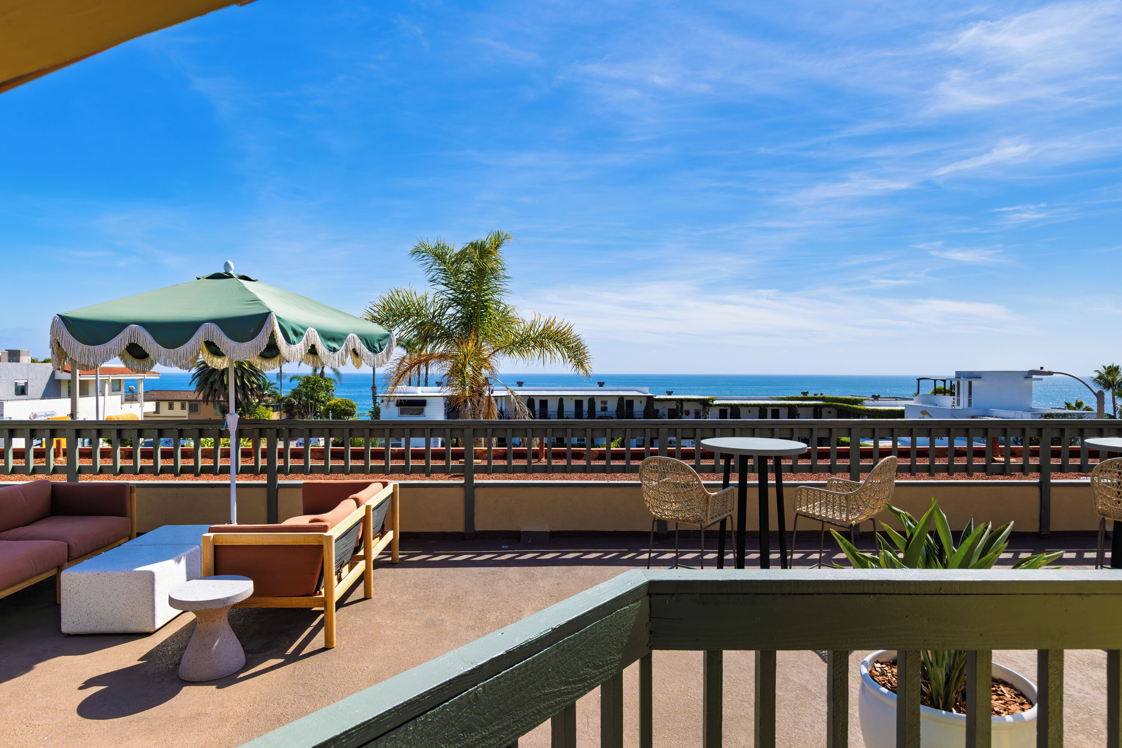 A terrace with outdoor seating, a view of the ocean, and a palm tree.
