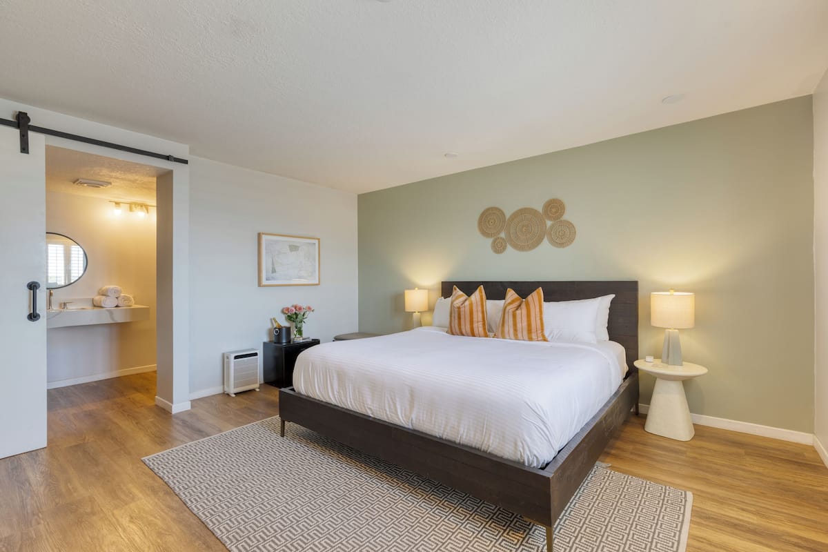 A bedroom with a bed, bedside lamps, a wall clock, and a small table with a lamp.