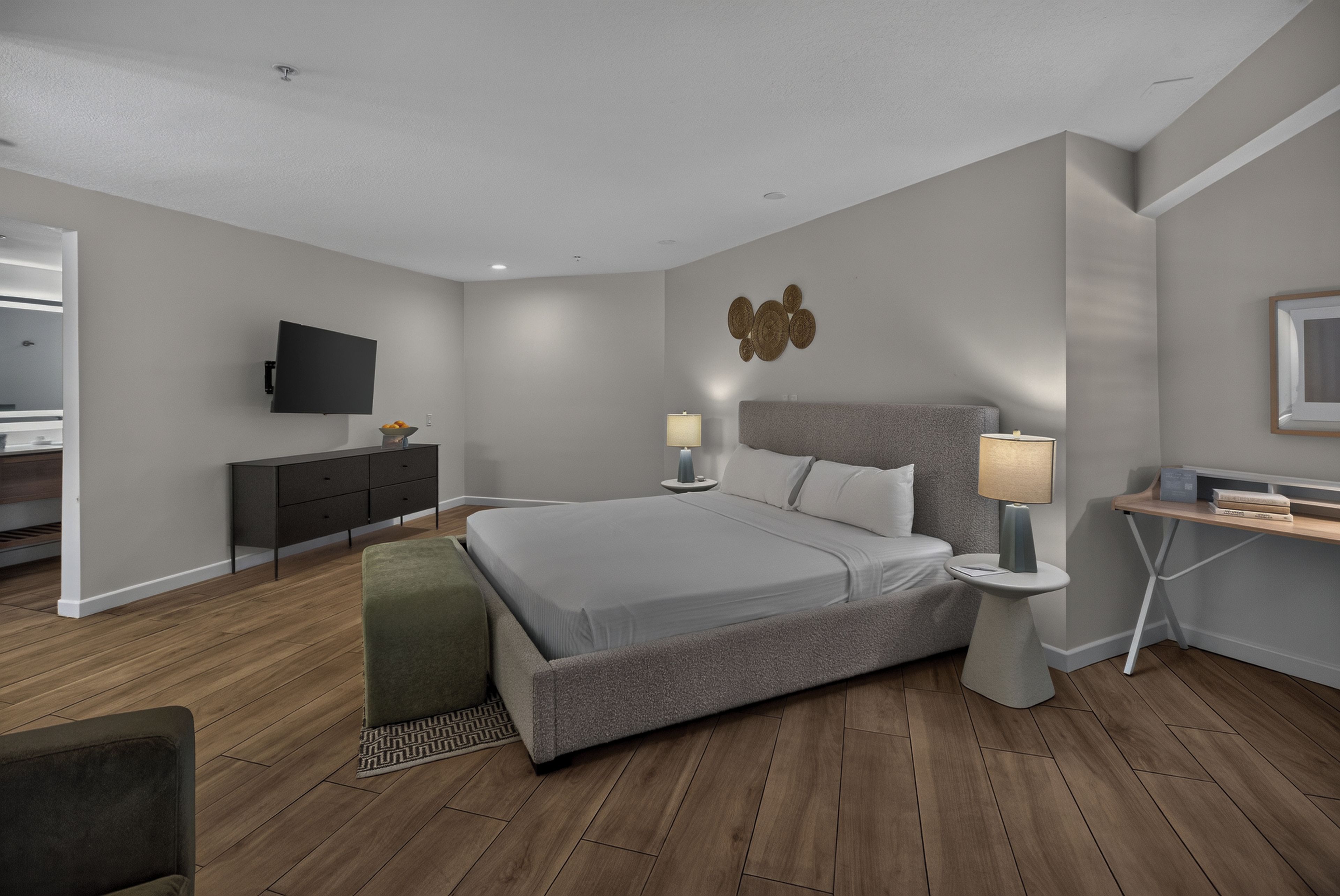 A modern bedroom with a large bed, bedside tables, a flat-screen TV, and a desk with a chair.