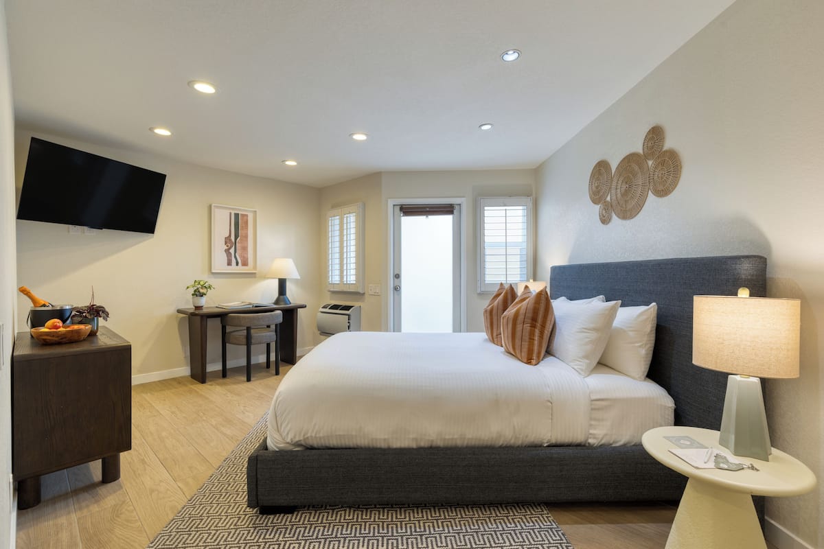 A modern hotel room with a large bed, a desk, a television, and a view of the outdoors.