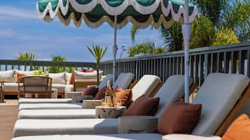 A row of sun loungers with a table and umbrella, a wicker chair, and a railing.
