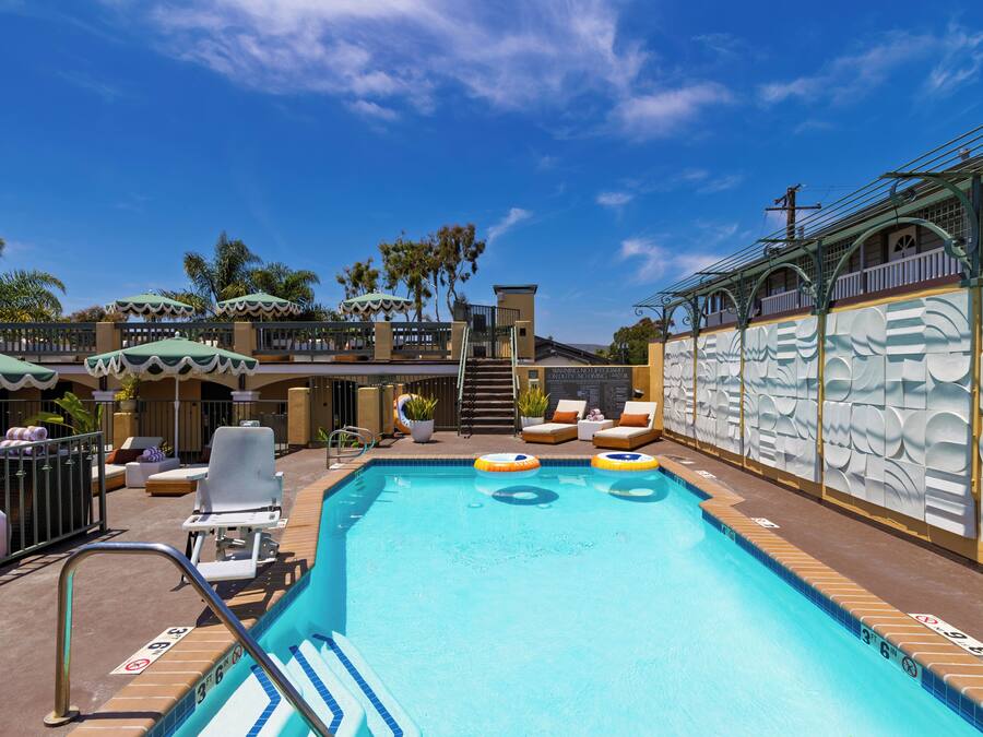 A swimming pool with lounge chairs and umbrellas, surrounded by palm trees and a building with a decorative facade.