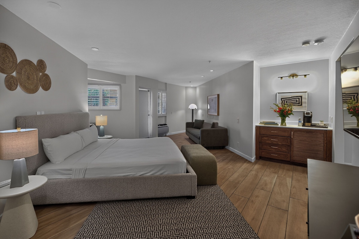 A modern bedroom with a large bed, bedside tables, a sofa, and a desk area.