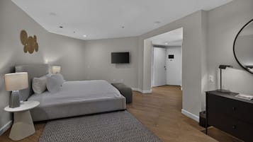A modern bedroom with a large bed, bedside lamps, a flat-screen TV, a dresser, and a mirror.