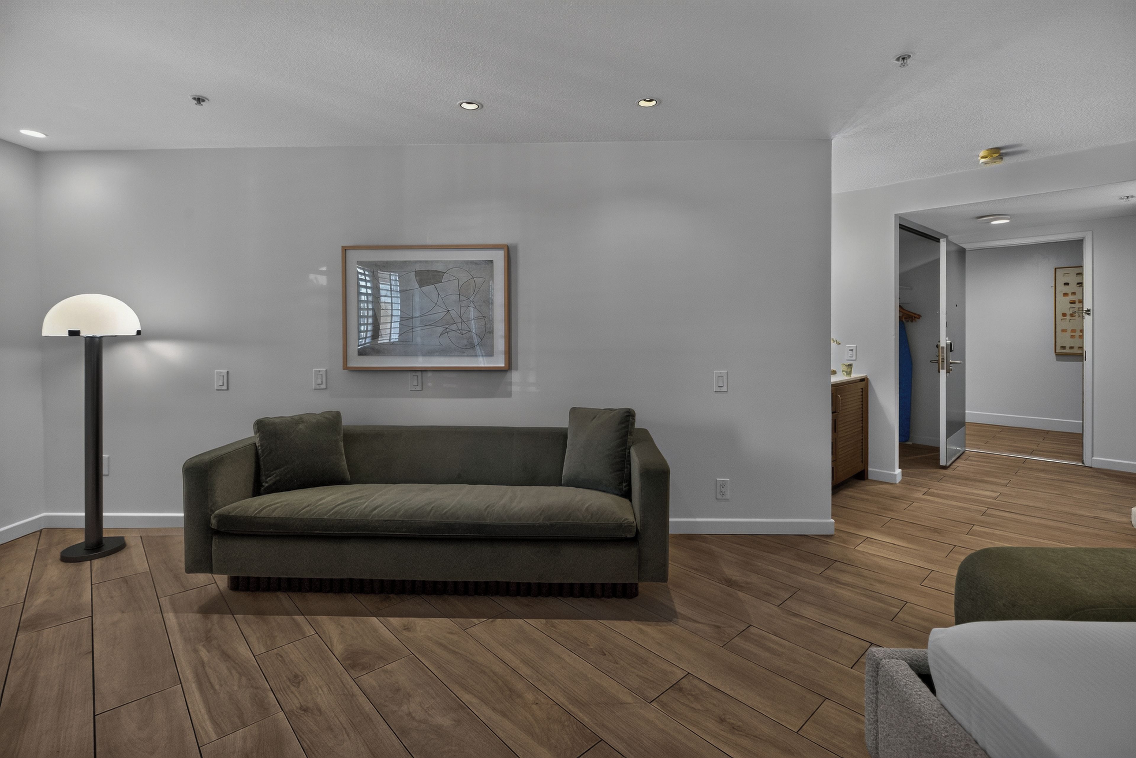 A modern living room with a grey sofa, a floor lamp, and a framed abstract artwork on the wall.