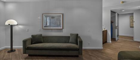 A modern living room with a grey sofa, a floor lamp, and a framed abstract artwork on the wall.