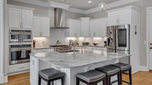 Una cocina moderna con armarios blancos, electrodomésticos de acero inoxidable, una isla de mármol y taburetes de bar.