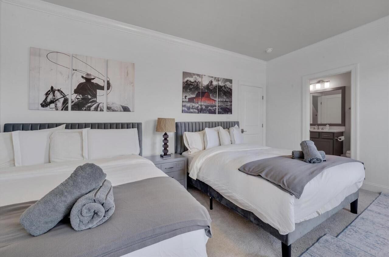 A bedroom with two beds, a nightstand, a lamp, and artwork on the walls.