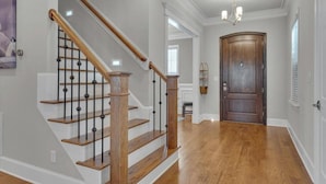 Una escalera con escalones de madera y barandillas negras, una puerta de madera y un candelabro.