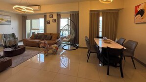 A modern living room with a sofa, a dining table with chairs, a hanging chair, and a large window.