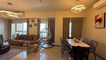 A modern living room with a sofa, a hanging chair, a dining table with chairs, and a large window.