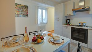 Een moderne keuken met een eettafel gedekt voor twee personen, met een fles, fruit en een schilderij aan de muur.