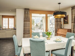 Ein Essbereich mit einem Tisch für sechs Personen, einer Chandelier und Blick auf einen verschneiten Berg.