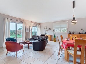 Een ruime woonkamer met een bank, stoelen, een eettafel en een keukenhoek.