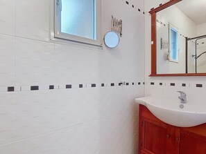 Ein Badezimmer mit weiß gefliesten Wänden, einem Holzwaschtisch, einem runden Spiegel und einem Fenster mit Milchglas.