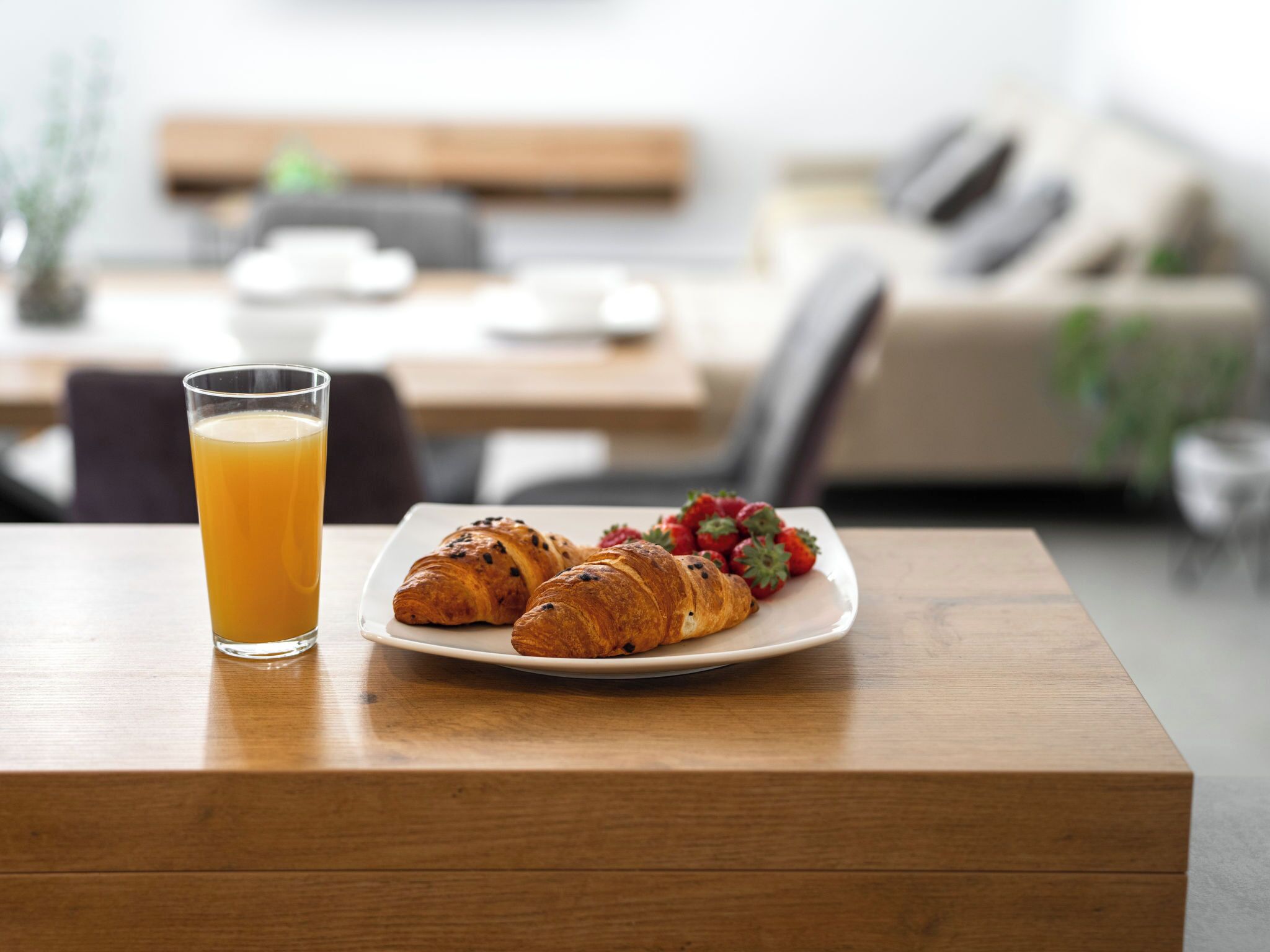 Un desayuno con una fuente de croissants y fresas, un vaso de jugo de naranja y una mesa de madera.