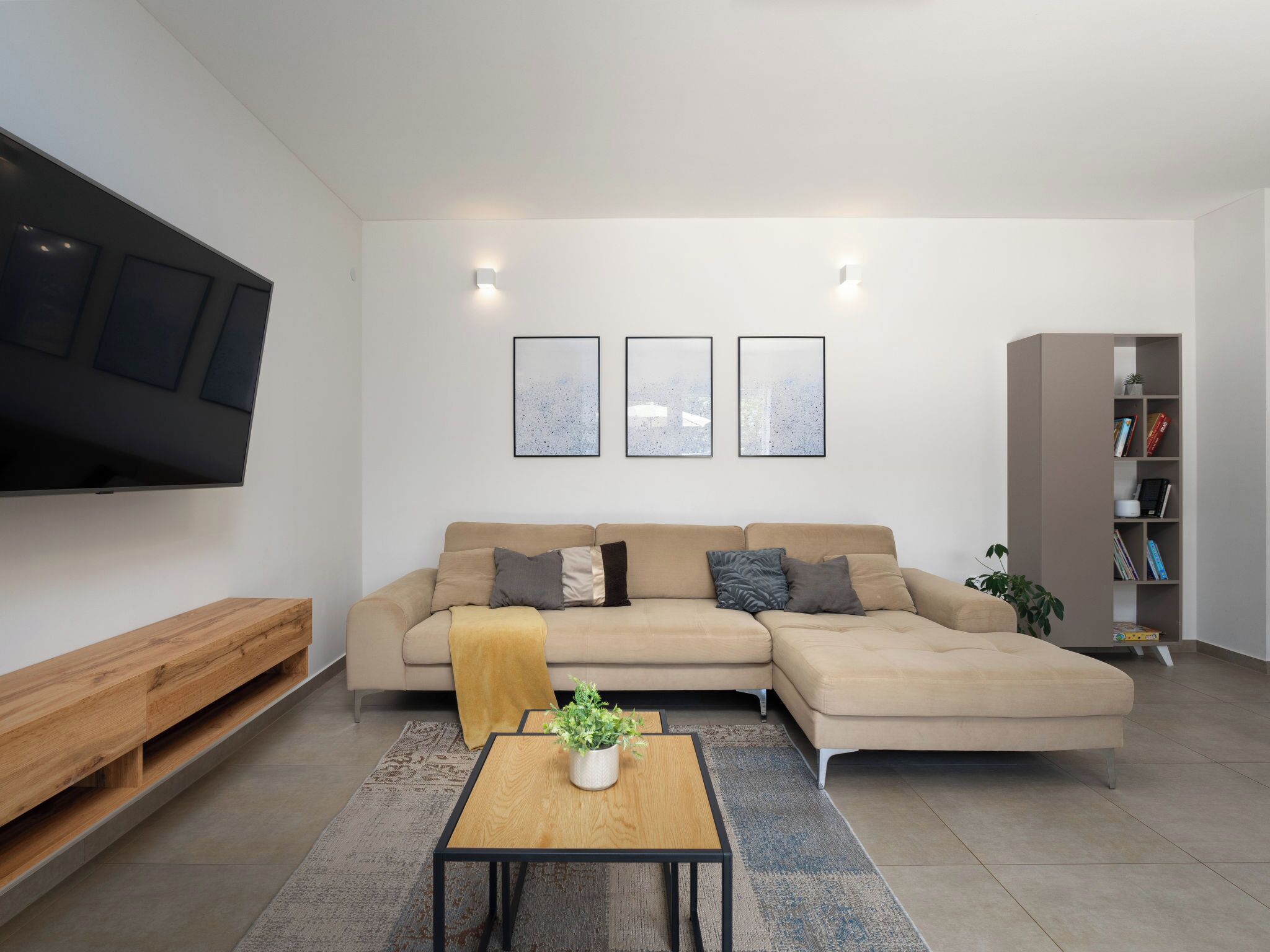 Een moderne woonkamer met een hoekbank, een flatscreen televisie, ingelijste kunstwerken, een houten salontafel en een boekenkast.