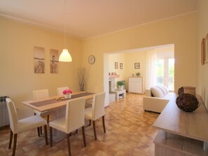 Ein Essbereich mit Holztisch und -stühlen, im Hintergrund eine Küche und ein Wohnbereich mit Sofa und einer dekorativen Schale.