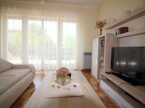 Ein Wohnzimmer mit einer Couch, einem Couchtisch mit Dekoration, einem Fernseher auf einem Holzgestell und einem Bücherregal.