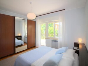 Ein Schlafzimmer mit Bett, Nachttisch, Spiegel und einem Fenster mit Vorhängen.