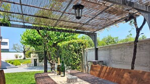 Eine Terrasse im Freien mit einem Holztisch, Stühlen, einer Pergola und einem an der Wand befestigten Grill.