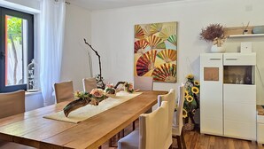 Ein Essbereich mit einem Holztisch, weißen Stühlen, einer Dekoration in der Mitte und einem Wandbild.