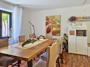 A dining area with a wooden table, white chairs, a decorative centerpiece, and a wall-mounted painting. - Villa Roza by Interhome (Umag)
