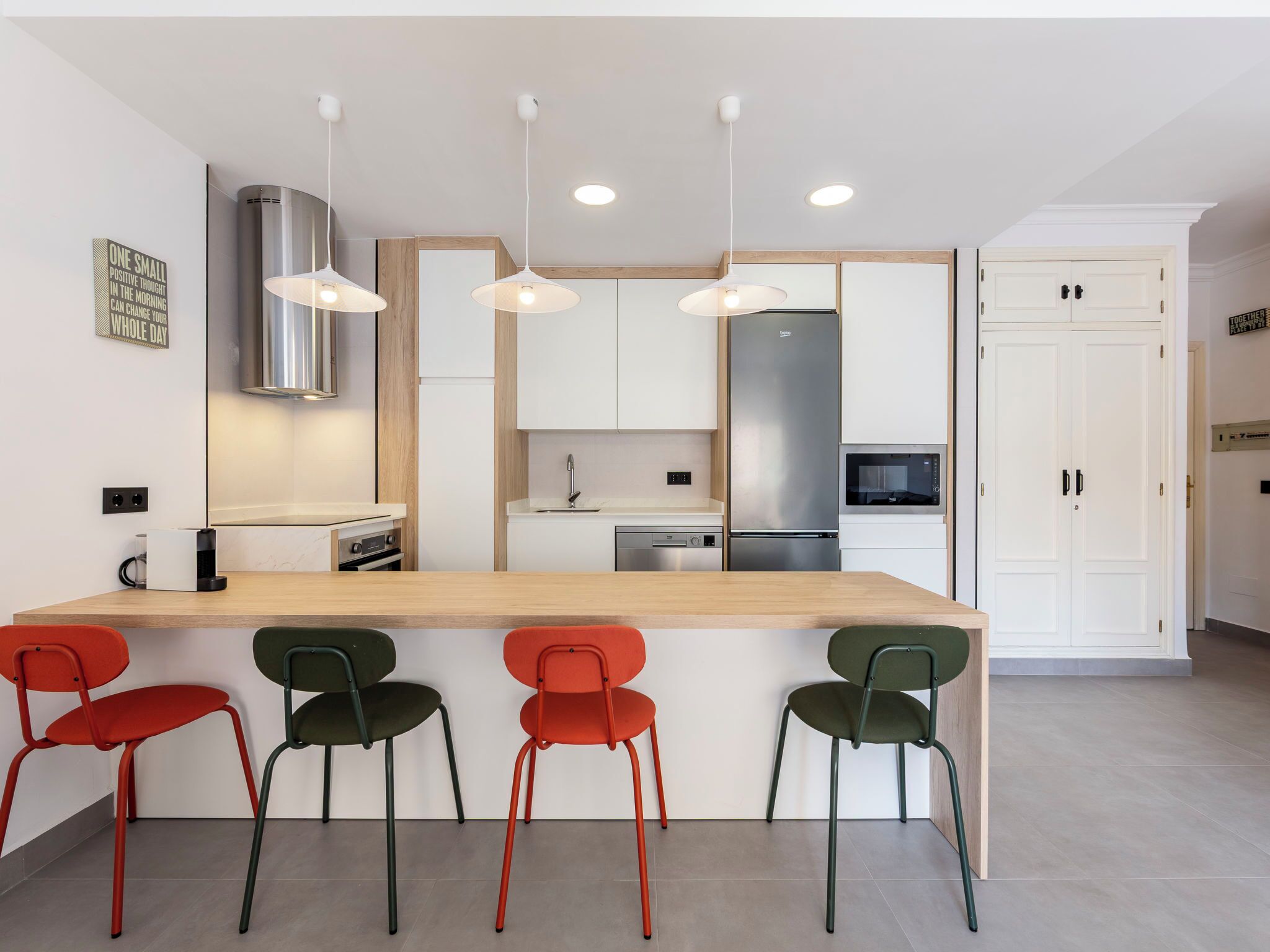 A modern kitchen with a central island, pendant lights, and a stainless steel refrigerator.