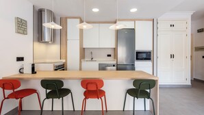 Une cuisine moderne dotée d’un îlot central, de luminaires suspendus et d’un réfrigérateur en acier inoxydable.