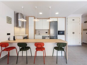 A modern kitchen with a central island, pendant lights, and a stainless steel refrigerator.
