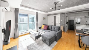 A modern living room with a grey sectional sofa, a flat-screen TV, and a dining area with a wooden table and chairs. - ANAX NORD 502 (Sapporo)