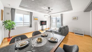 A modern dining area with a table set for four, a potted plant, and a flat-screen TV displaying Netflix. - ANAX NORD 502 (Sapporo)