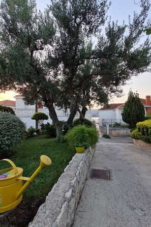 A garden with a yellow watering can, a stone wall, and a tree. - Charmante Wohnung Jasmine 1 in Strandnähe by Interhome (Trogir/Okrug Donji)