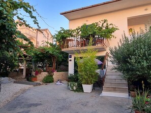 Ein zweistöckiges Gebäude mit Balkon, umgeben von Grünpflanzen und Topfpflanzen.