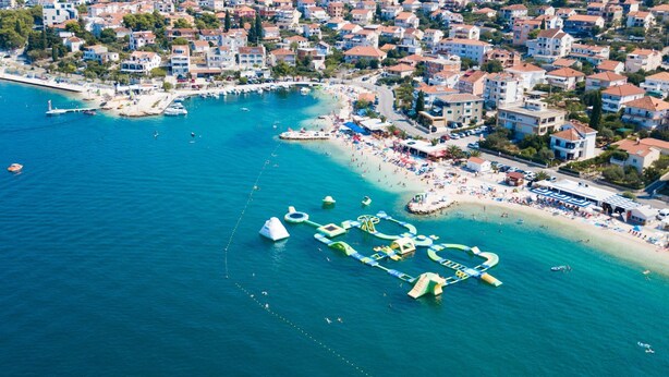 Vista aérea de un pueblo costero con playa, barcos y puerto deportivo.