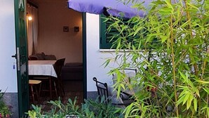 Un área de estar al aire libre con una mesa y sillas, rodeada de plantas en macetas y una planta de bambú.