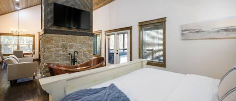 Ein Schlafzimmer mit einem großen Bett, einem Kamin aus Stein, einer Badewanne und Blick ins Freie.