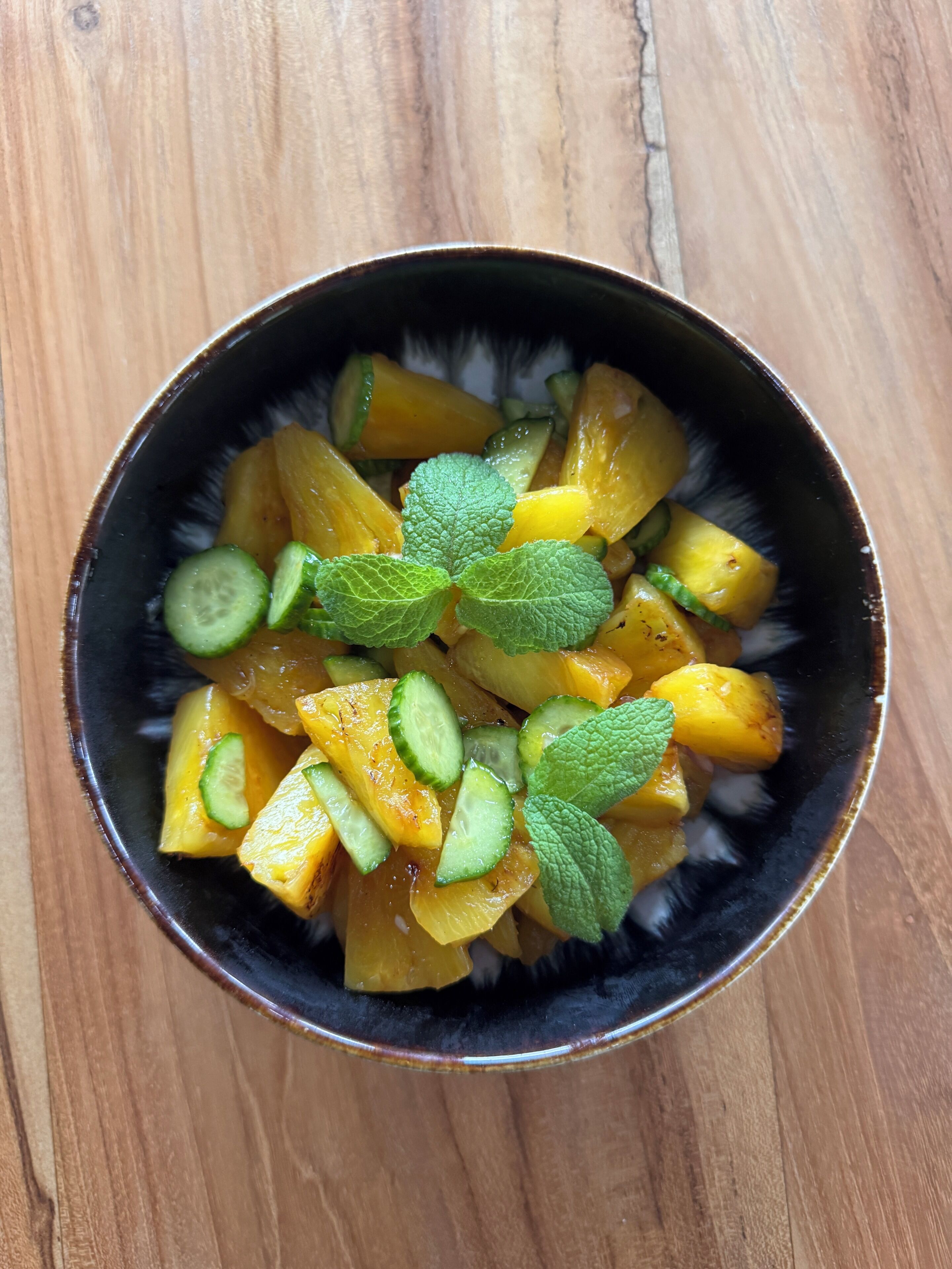 A bowl of fruit salad with mint leaves on a wooden surface.