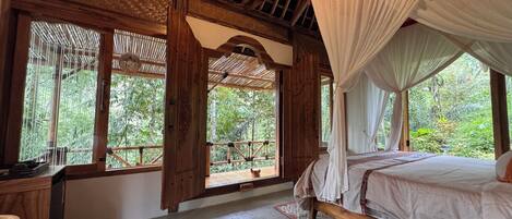 Quarto com uma cama, um banco de madeira, uma janela com vista para áreas verdes e uma cama com dossel.
