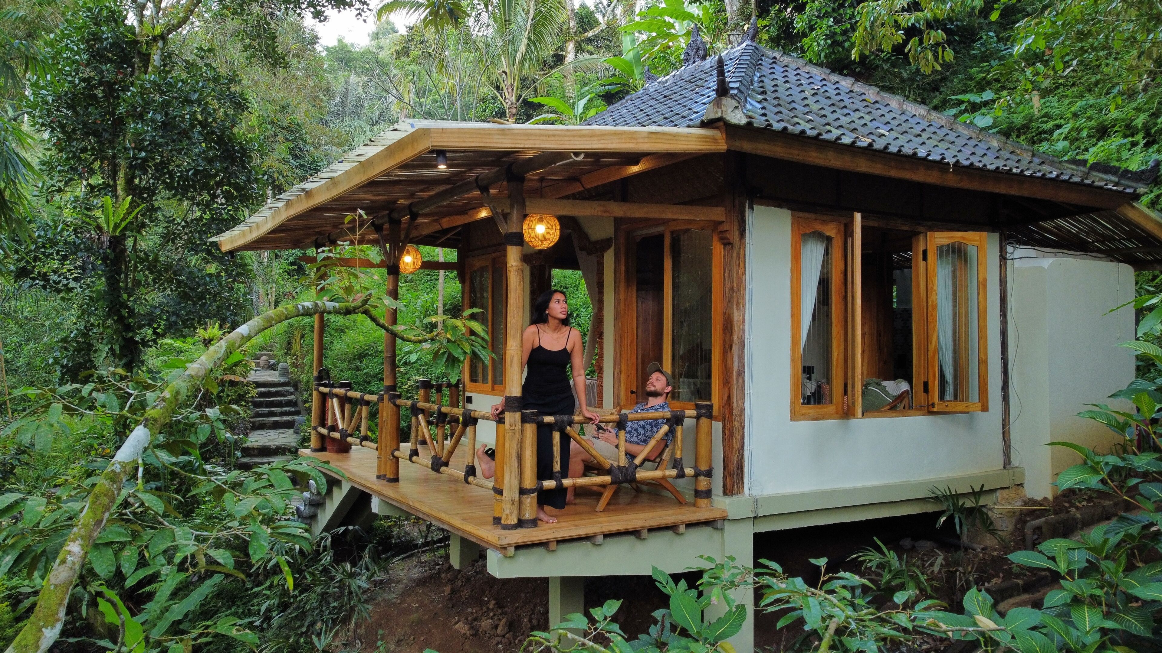 Uma cabana de madeira com varanda, rodeada por vegetação exuberante.