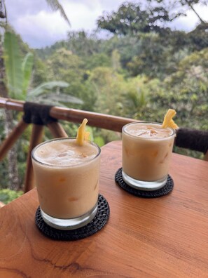 Dos vasos de bebida helada sobre una mesa de madera, con vistas a un paisaje boscoso.