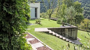 Una casa con un pequeño jardín delantero, una escalera de piedra y vistas a una montaña boscosa.