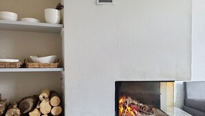 Una chimenea con leña, un estante con vajilla y una pila de leña.