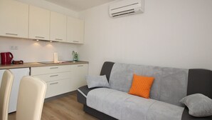 A compact living space with a kitchenette, a sofa with cushions, a chair, and an air conditioning unit. - Apartments Ivo by Interhome (Polje)