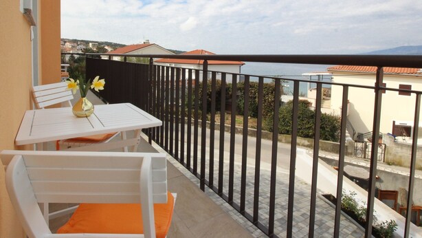 A balcony with a white table and chair, a vase with flowers, and a view of the sea and buildings. - Apartments Ivo by Interhome (Polje)