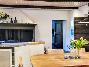 Une cuisine moderne dotée d’un îlot central intégré, un coin repas avec une table et des chaises en bois, et une porte-fenêtre donnant sur une autre pièce.