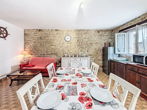 Un coin repas avec une table dressée pour quatre personnes, une chaise rouge, un mur en pierre et une horloge accrochée au mur.