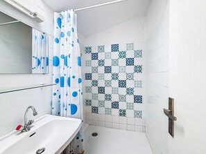 Une salle de bain avec un lavabo blanc, un miroir, une douche avec un rideau à pois bleus et des carreaux décoratifs sur les murs.